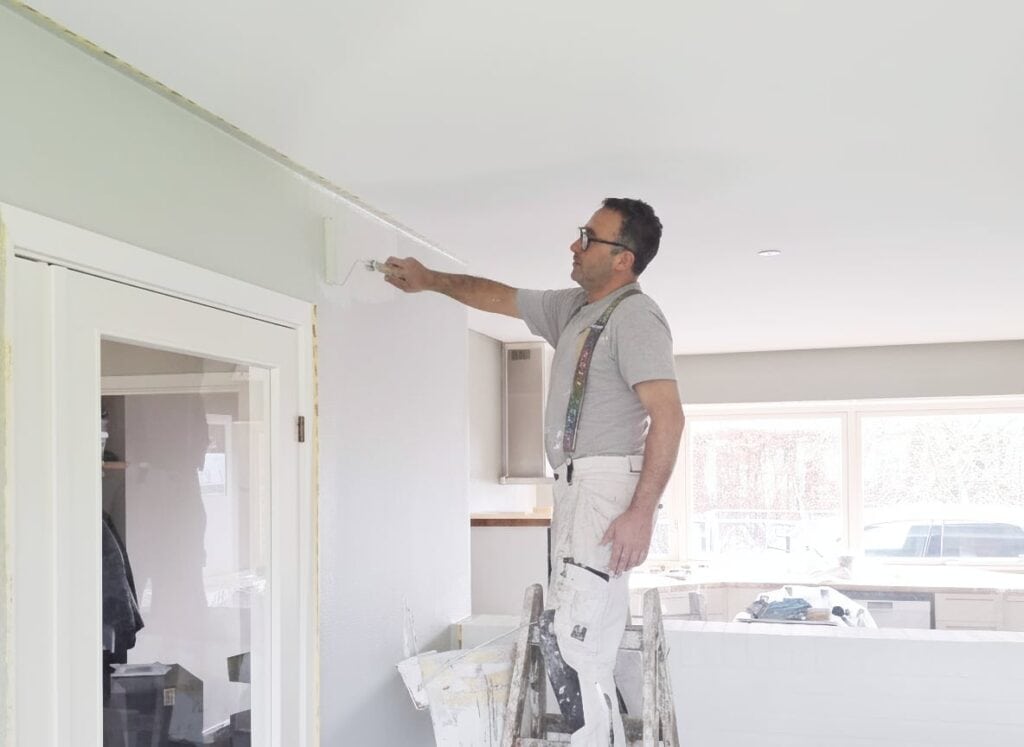 Maler, der maleser væg med pensel i et indendørs rum under renovering.