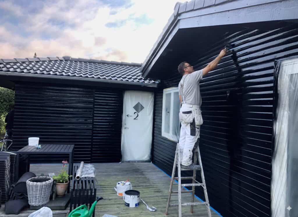 Maler arbejder på sort træfacade på udendørs hus, fornyelse med sort maling, professionel malertjeneste, Svane Maler.